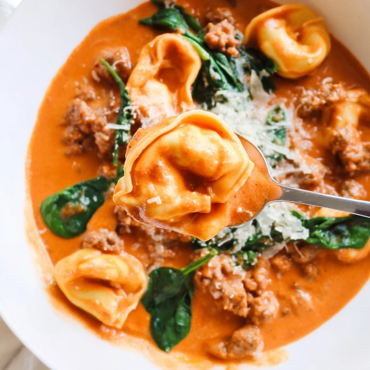 Creamy Tuscan Tortellini Soup with sausage and spinach, garnished with Parmesan and herbs in a rustic bowl.