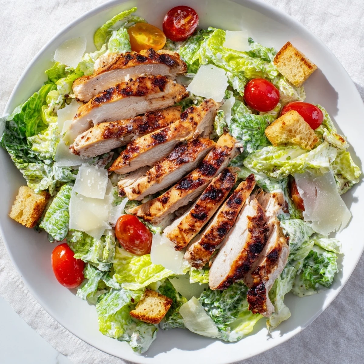 Close-up of tender grilled chicken strips on a bed of crisp romaine lettuce, smothered in a creamy yogurt Caesar dressing. Finished with homemade croutons and shaved Parmesan for a high-protein meal.