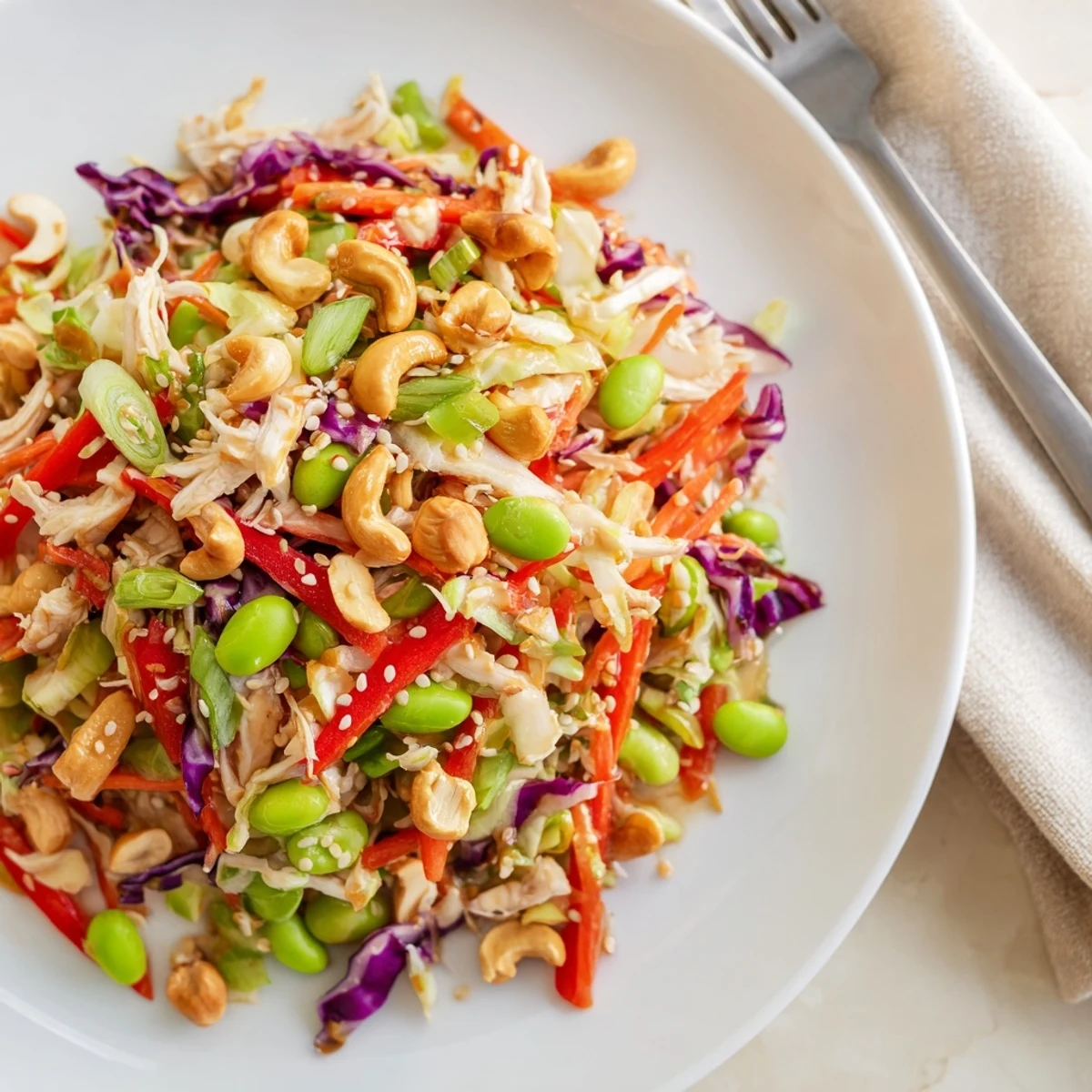 Vibrant Edamame Crunch Chicken Salad served in a white bowl, topped with toasted sesame seeds and crunchy cashews for texture.