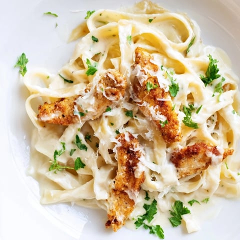 Freshly sliced Cajun chicken rests atop creamy Alfredo fettuccine, garnished with chopped parsley and extra Parmesan cheese.  