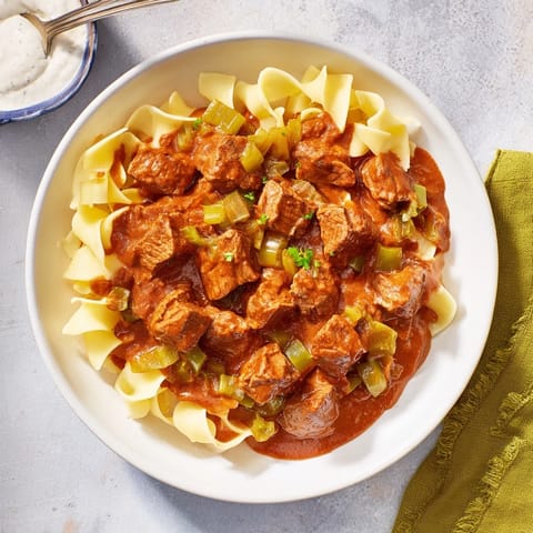 A steaming bowl of Hungarian Goulash, the tender beef and vibrant sauce glistening over buttery noodles.