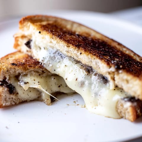 Freshly made Truffle Grilled Cheese on a plate, served with a side of salad and a glass of white wine.
