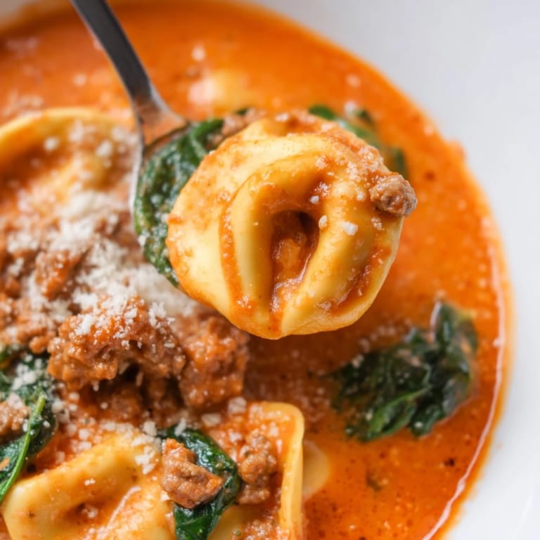 Steamy bowl of Tuscan Tortellini Soup featuring cheesy tortellini, browned sausage crumbles, and wilted spinach leaves.