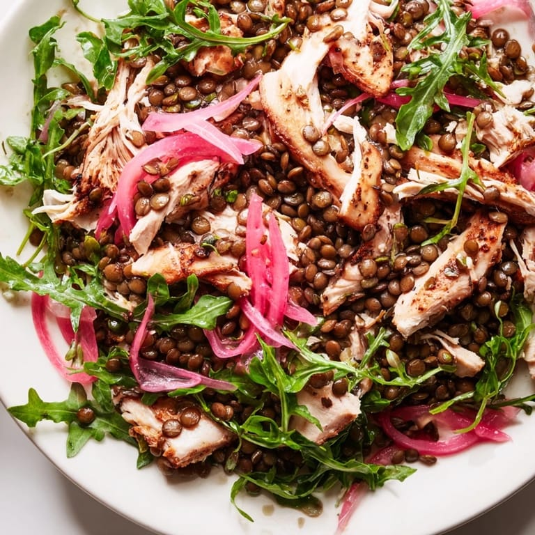 A protein-packed Lentil & Chicken Spring Salad served in a white bowl, featuring juicy roasted chicken and fresh vegetables on a rustic table.