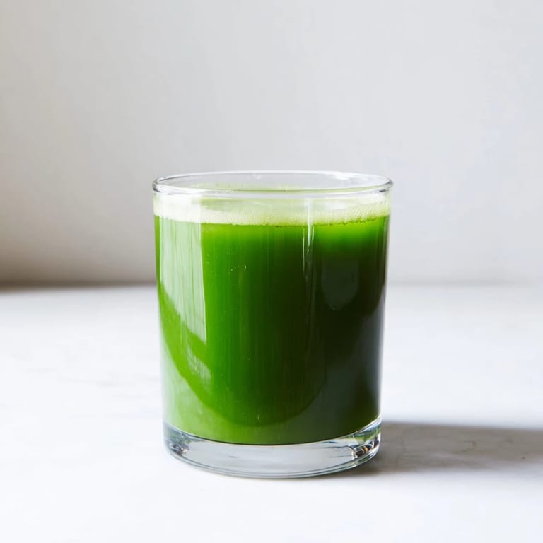 A tall glass of Cabbage and Kale Detox Juice showing a bright green hue, fresh kale leaves, and a lemon slice on the rim.  